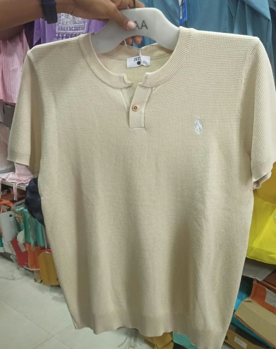 a cream-colored short-sleeve textured knit Henley shirt featuring a single-button placket and a small embroidered logo on the chest.